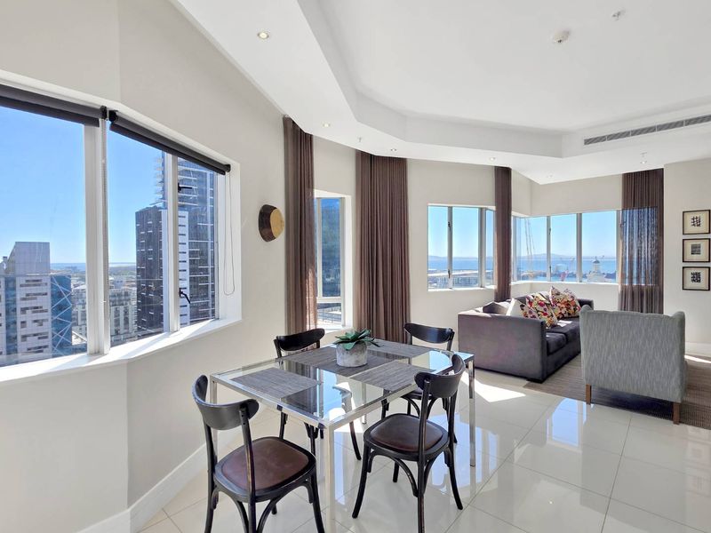 Bright open-plan living and dining area featuring large windows with expansive city and ocean views, high-gloss floor tiles, and modern recessed ceiling lighting.