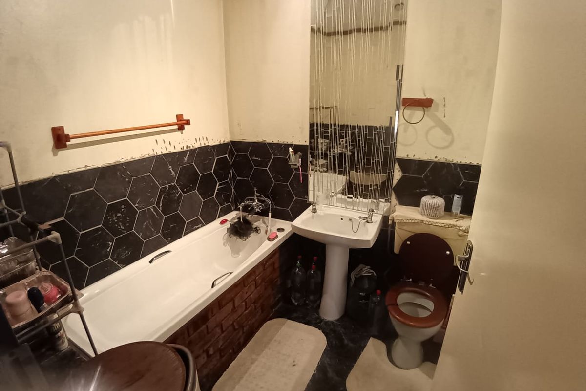 A dated bathroom featuring a bathtub with brick-style base, pedestal basin, and toilet, currently requiring cosmetic updates and tile repairs.