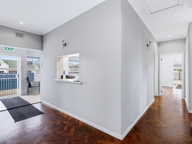 A bright, spacious hallway featuring classic herringbone parquet flooring, a convenient serving hatch, and direct access to the exterior via a security gate.