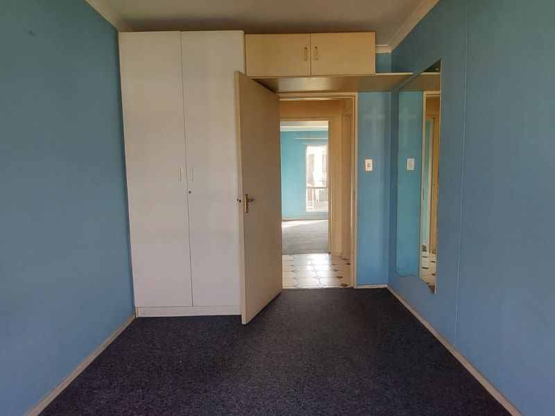 An empty bedroom featuring built-in cupboards, overhead storage, and a wall-mounted mirror, with direct access to an adjacent hallway.
