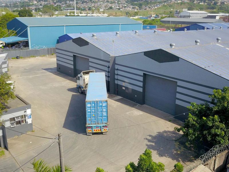 Aerial view of an industrial warehouse complex featuring large roller shutter doors, metal roofing, and a spacious concrete yard for logistics and vehicle access.