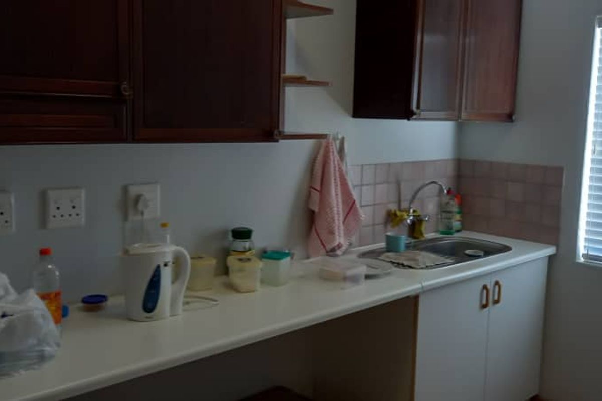 A functional kitchenette area featuring built-in wooden cabinetry, a stainless steel sink, and a tiled splashback with natural light from a window.