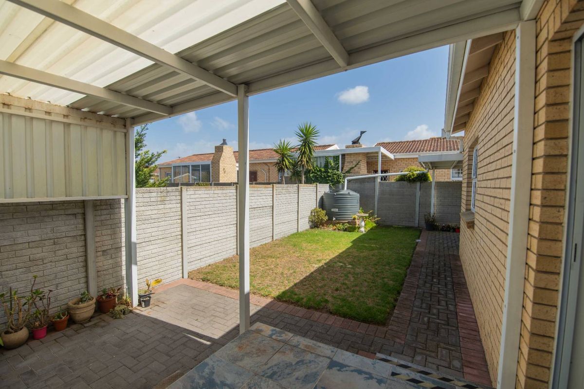 A private rear courtyard featuring a covered patio area, paved walkways, a small lawn, and a water storage tank enclosed by perimeter walls.