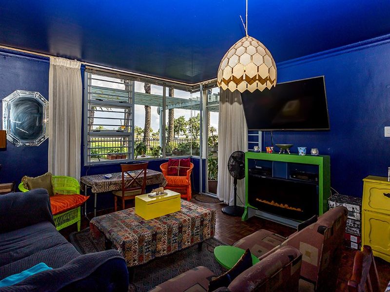 A living room featuring parquet flooring, louvered windows with garden views, and a built-in electric fireplace, finished with bold wall and ceiling paint.