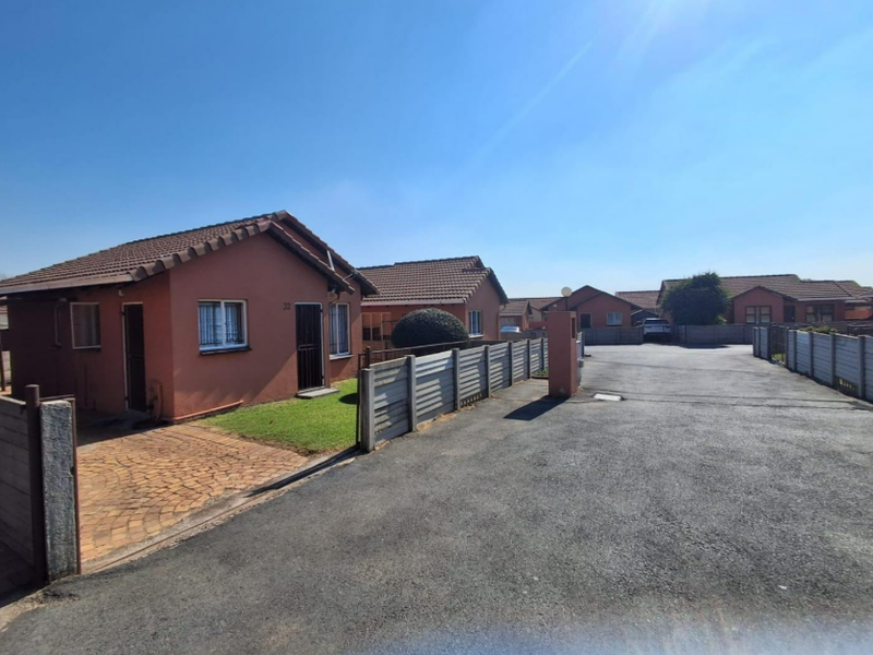 Front exterior view of a residential property featuring a tiled roof, paved driveway, and perimeter precast concrete walling within a complex setting.