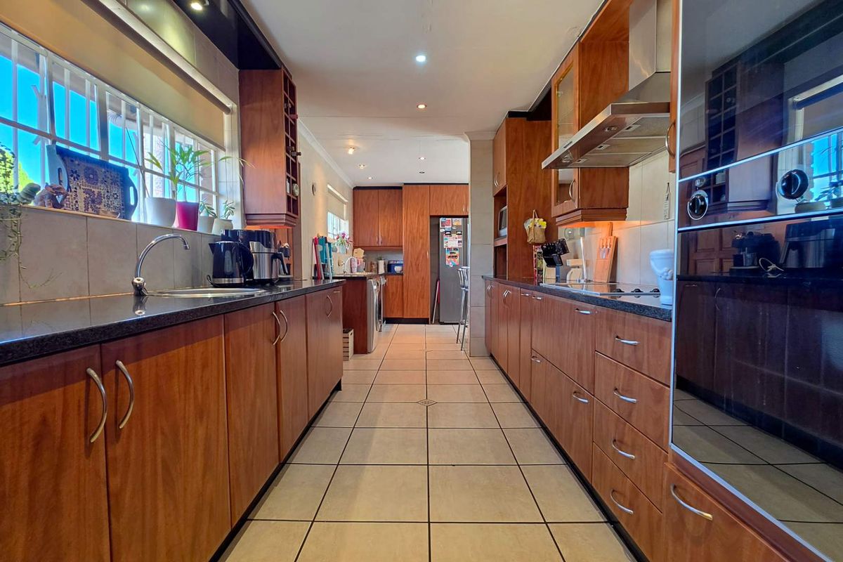 A galley-style kitchen featuring wood-finish cabinetry, dark granite countertops, tiled flooring, and integrated oven and extractor fan.