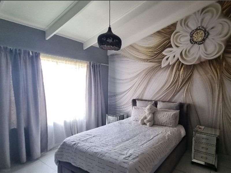 A well-maintained bedroom featuring exposed ceiling beams, tiled flooring, and a decorative feature wall with a modern pendant light fixture.