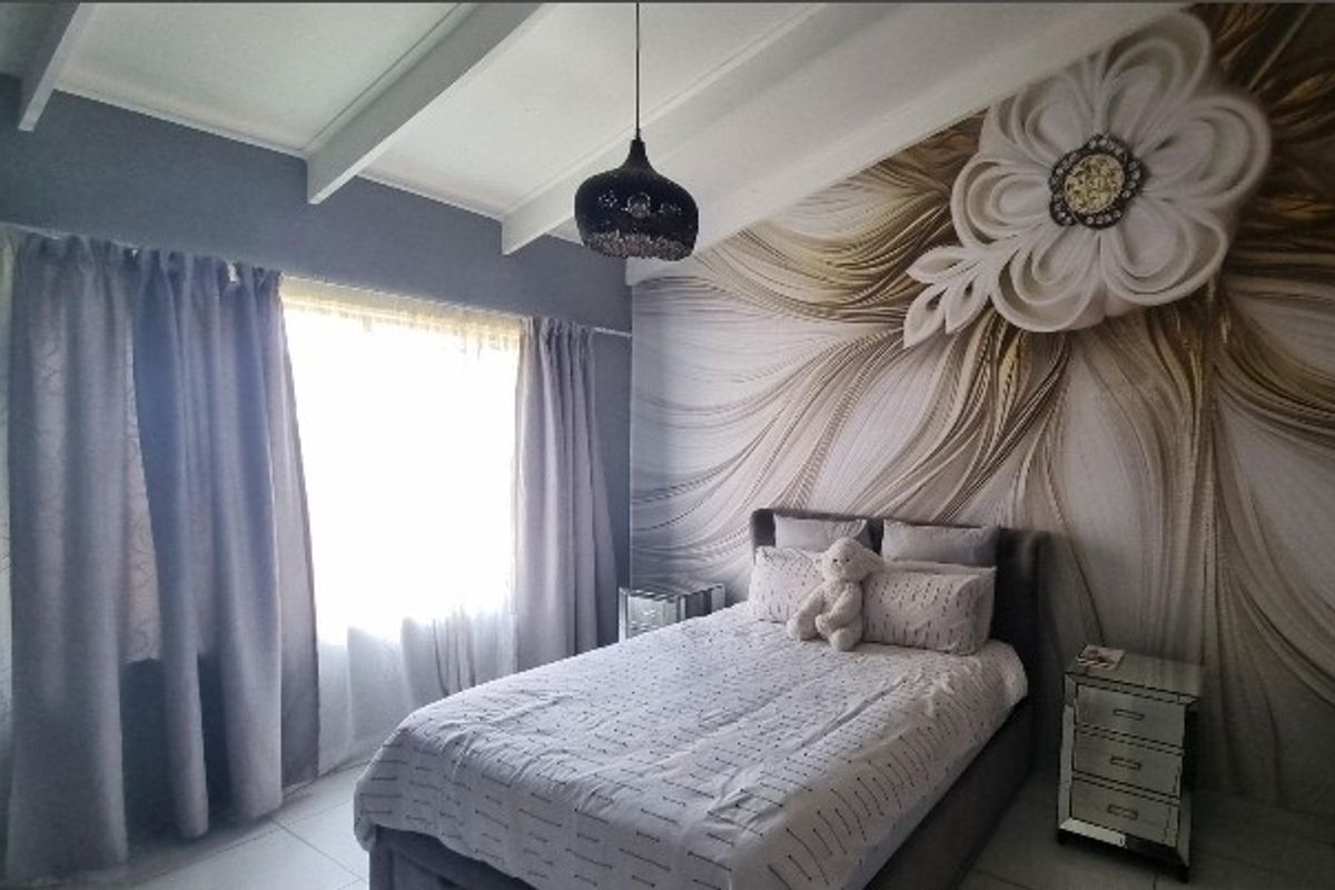 A well-maintained bedroom featuring exposed ceiling beams, tiled flooring, and a decorative feature wall with a modern pendant light fixture.