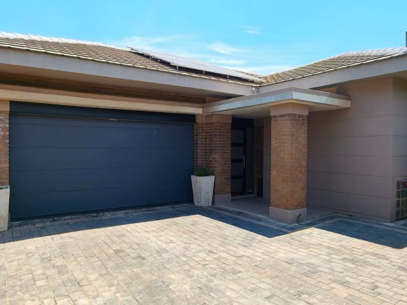 Front elevation of a modern house featuring a double garage, paved driveway, brick accents, and solar panels on the roof.