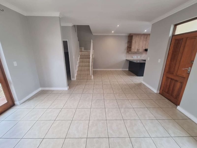 Spacious open-plan living area featuring tiled floors, a staircase, and a functional kitchen with granite countertops and wooden cabinetry.