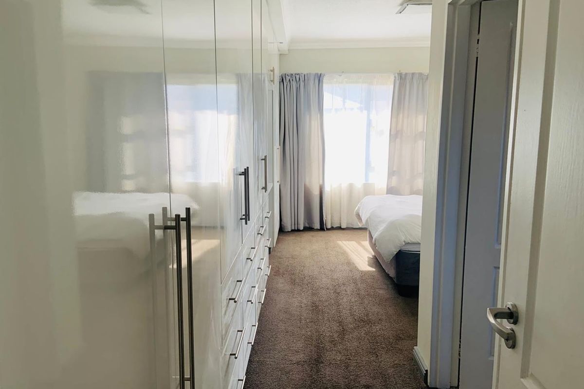 A bedroom featuring extensive built-in high-gloss cabinetry with ample storage space, carpeted flooring, and natural light from the window.