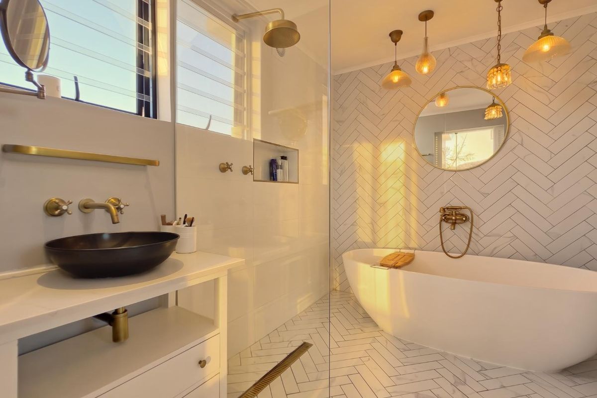 Modern bathroom featuring a freestanding bathtub, walk-in shower with brass fixtures, herringbone tiling, and a stylish vessel sink vanity.