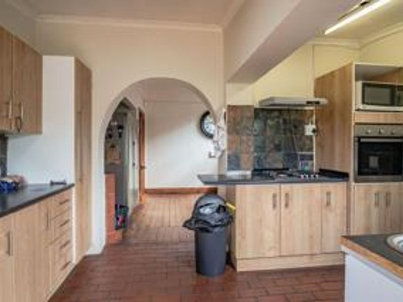 A functional kitchen featuring light wood-tone cabinetry, built-in oven and microwave, dark tiled backsplash, and terracotta-style floor tiles with an arched transition to the hallway.