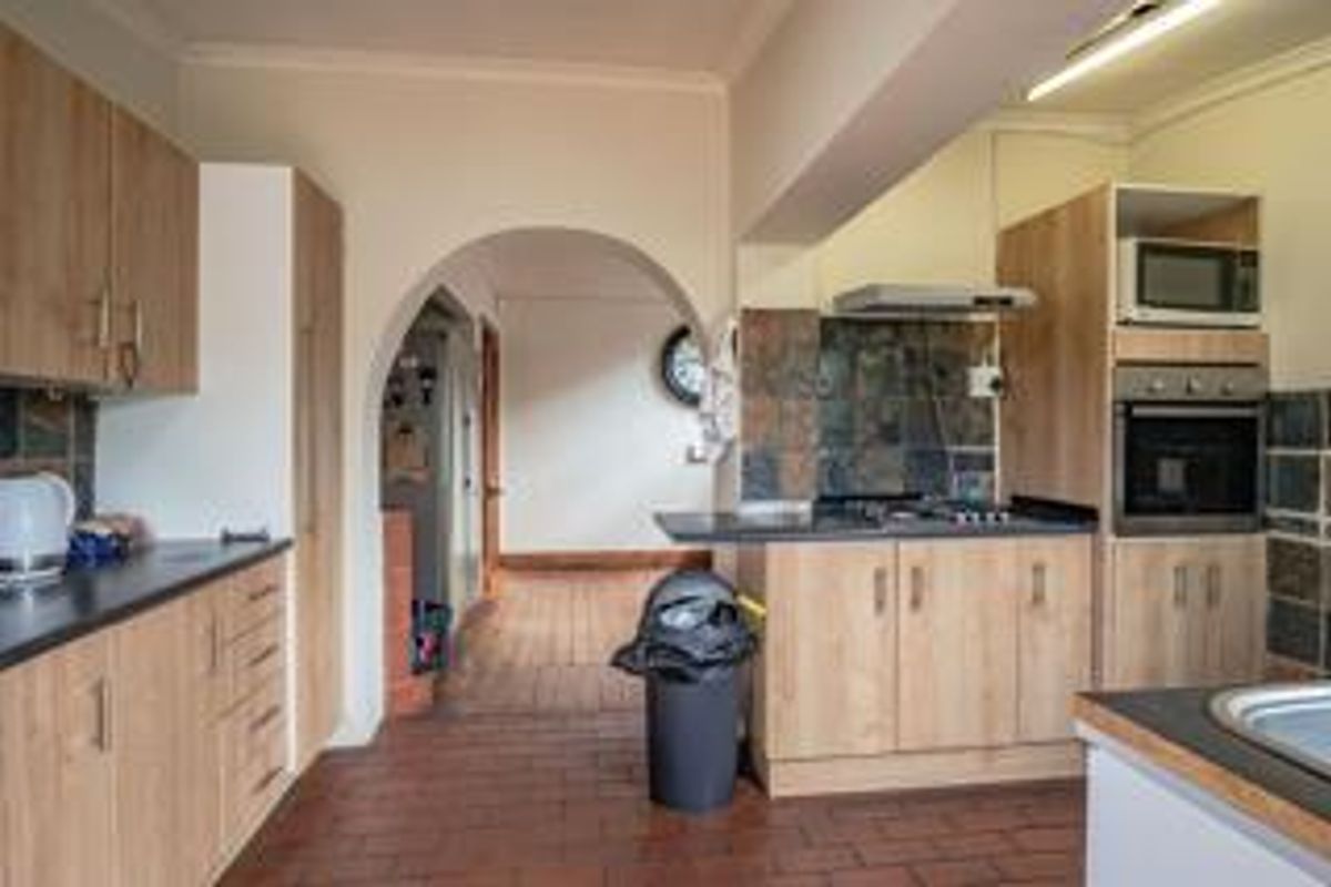 A functional kitchen featuring light wood-tone cabinetry, built-in oven and microwave, dark tiled backsplash, and terracotta-style floor tiles with an arched transition to the hallway.