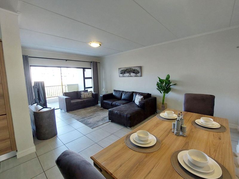 An open-plan living and dining area featuring tiled flooring, neutral walls, and a large sliding glass door leading to an outdoor balcony.