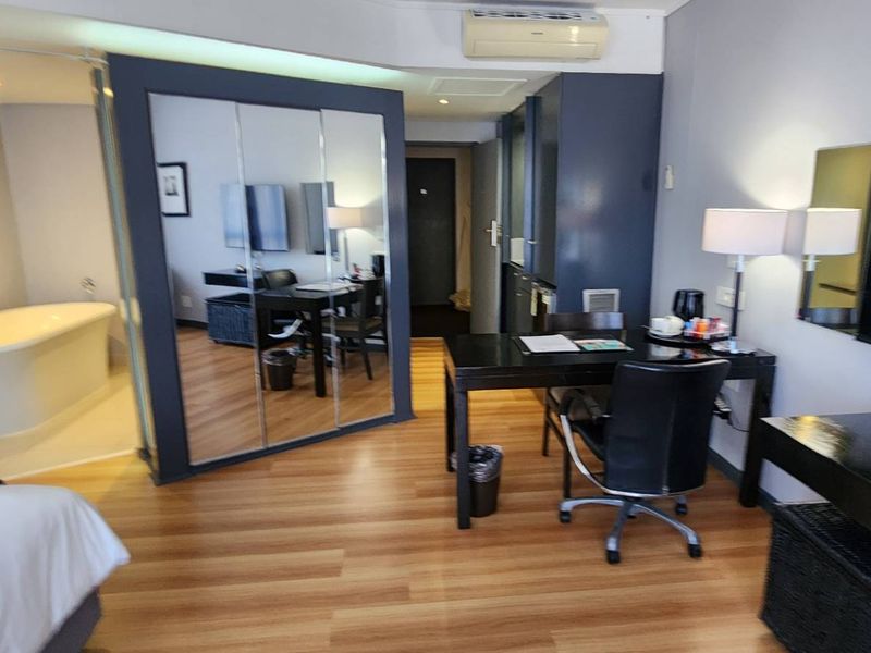 A modern bedroom suite featuring an open-plan layout with an integrated freestanding bathtub, mirrored wardrobe, and laminate flooring.