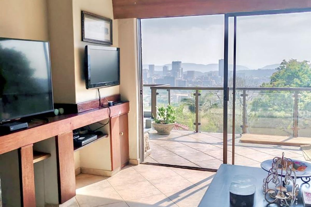 Living room featuring exposed timber ceiling beams, tiled flooring, and large sliding glass doors opening onto a balcony with expansive city views.