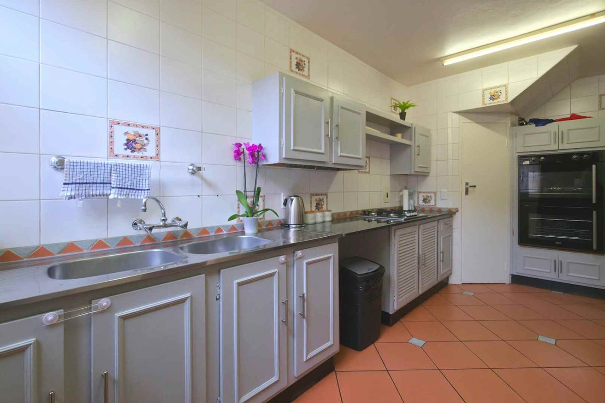 A functional kitchen featuring built-in cabinetry, a double stainless steel sink, integrated oven, and tiled flooring with wall-mounted splashback tiles.