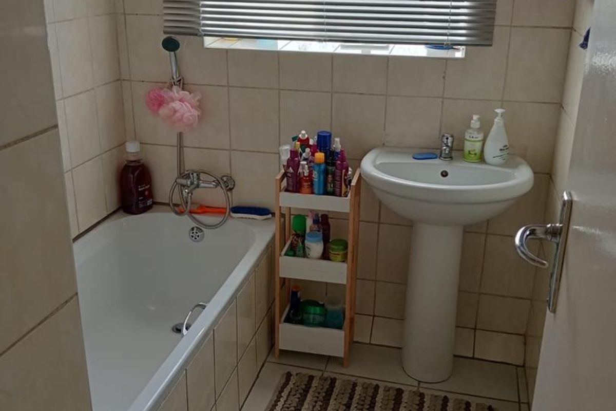 A functional bathroom featuring a standard bathtub with shower mixer, pedestal basin, and tiled walls and flooring.