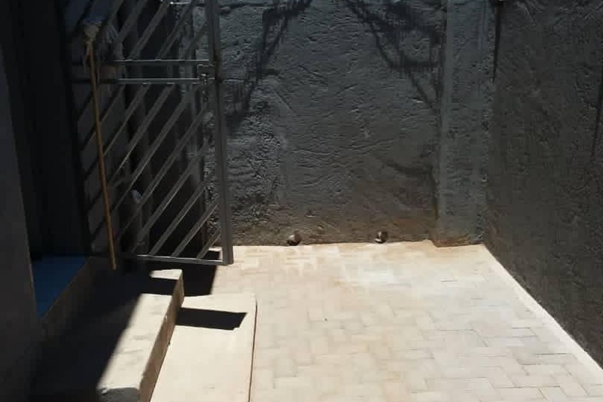 A small, paved rear courtyard area enclosed by high perimeter walls with security razor wire and a metal security gate.