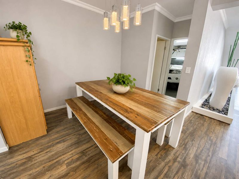 A bright dining area featuring wood-look laminate flooring, crown molding, and modern pendant lighting, with an open transition to the garage area.
