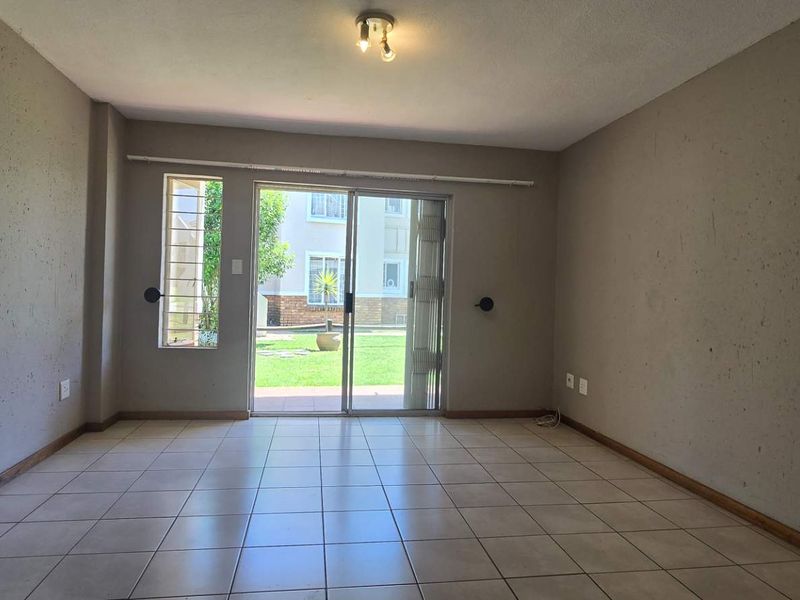 An empty living room featuring tiled flooring and a sliding glass door that provides access to the outdoor area.