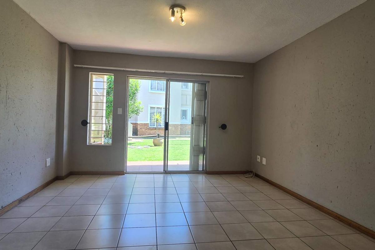 An empty living room featuring tiled flooring and a sliding glass door that provides access to the outdoor area.