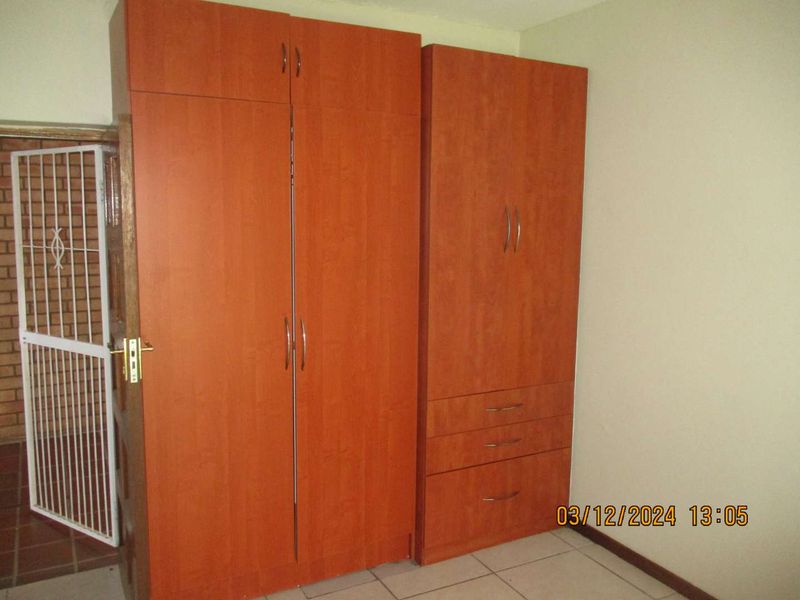 A bedroom featuring built-in wooden cupboards, tiled flooring, and a security gate at the entrance.