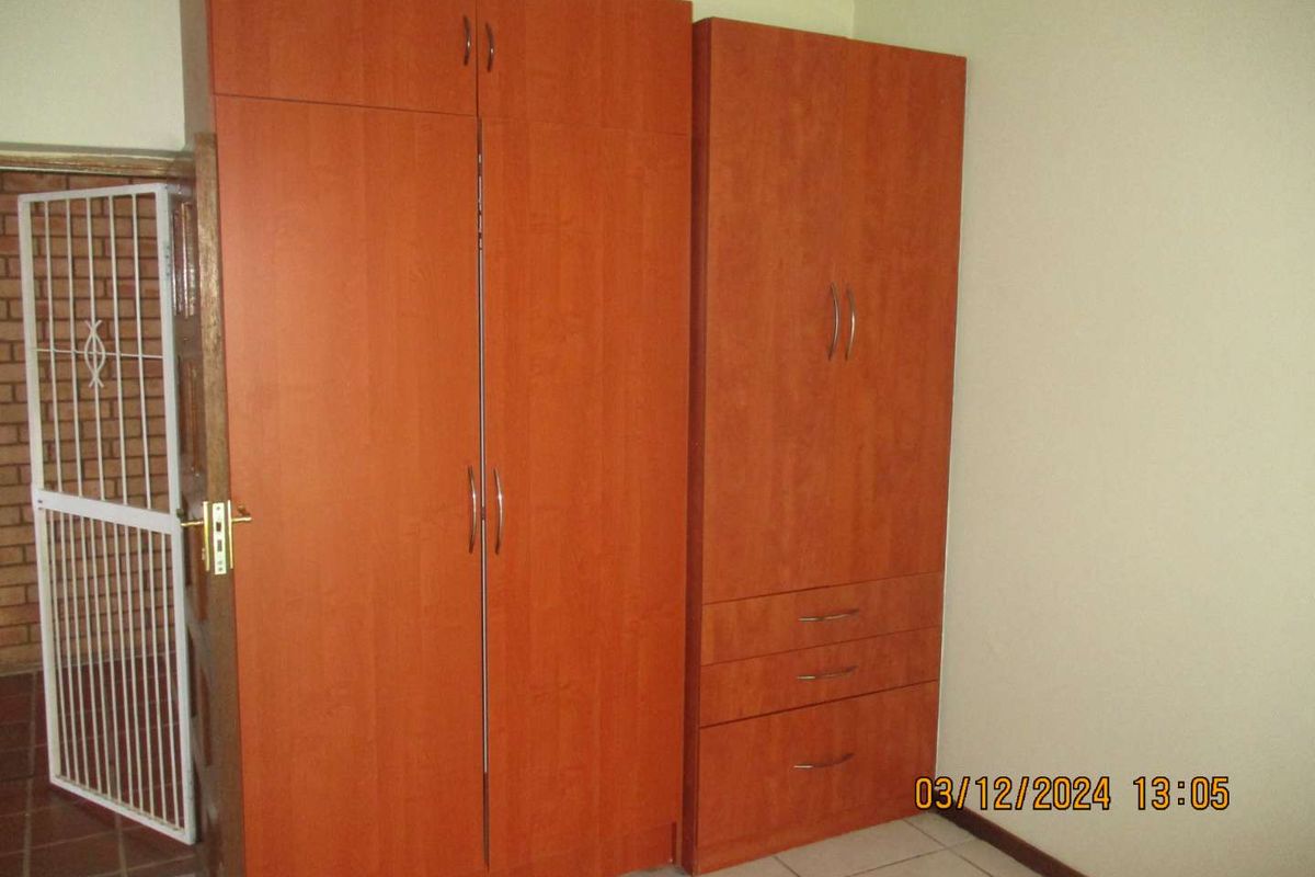 A bedroom featuring built-in wooden cupboards, tiled flooring, and a security gate at the entrance.