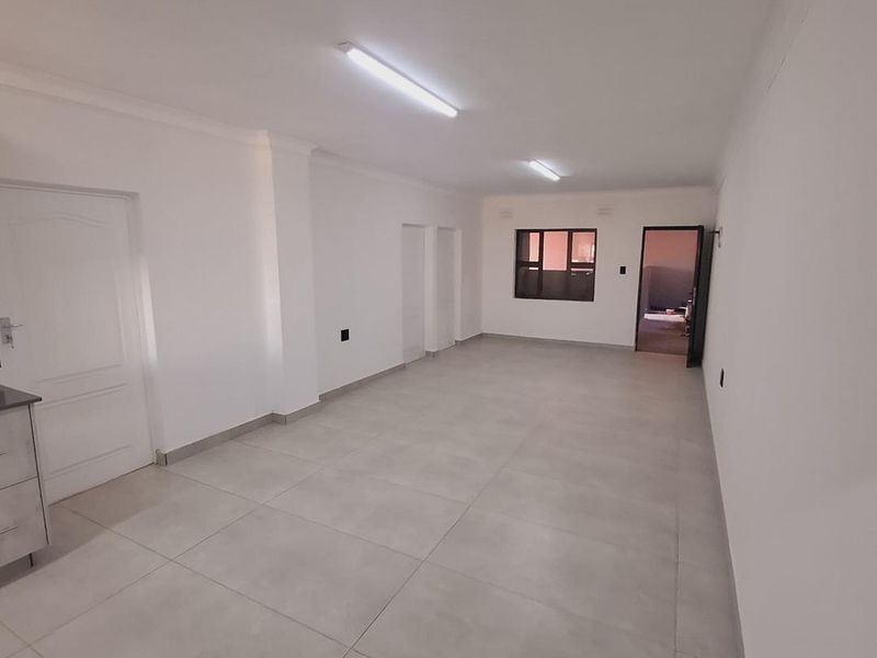 A spacious, empty living area featuring neutral tiled flooring, clean white walls, and functional overhead lighting, ready for personalization.