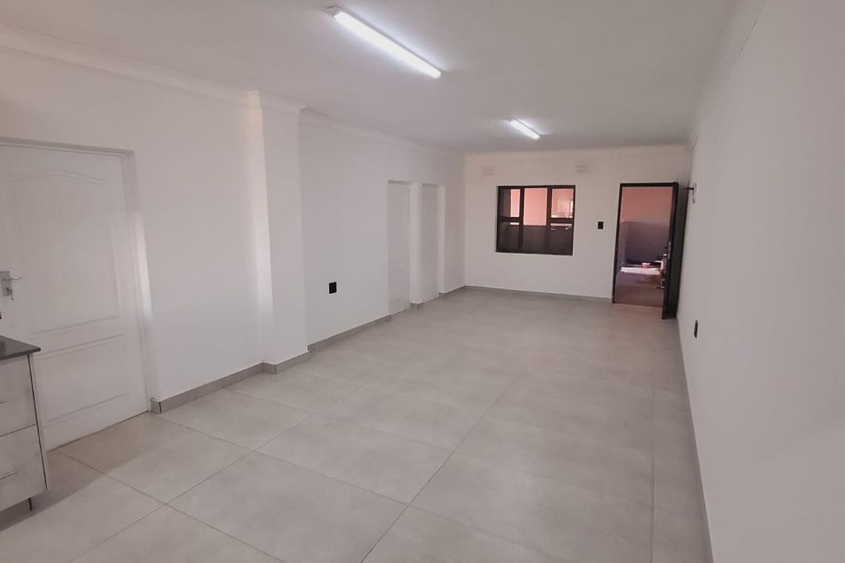 A spacious, empty living area featuring neutral tiled flooring, clean white walls, and functional overhead lighting, ready for personalization.