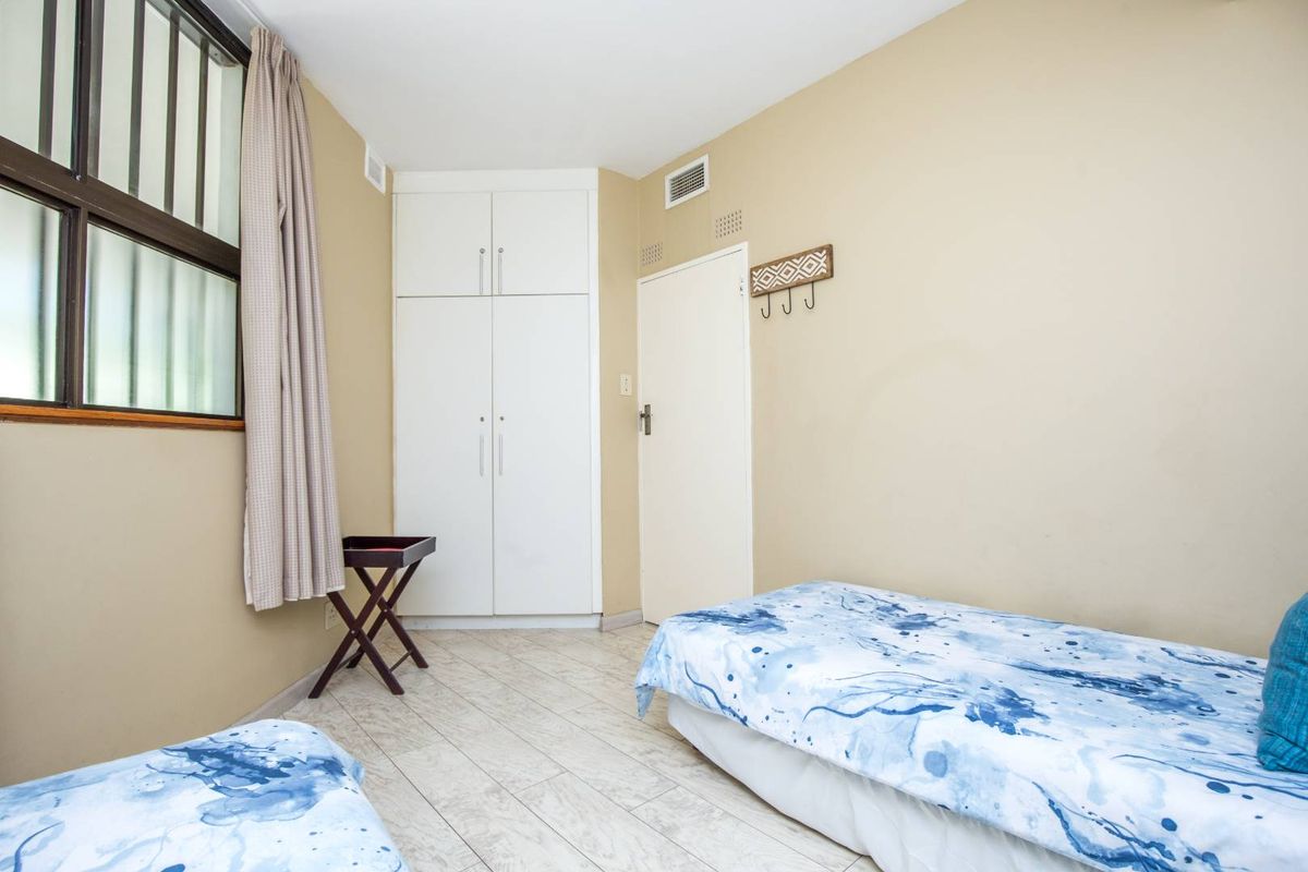 A bedroom featuring built-in white cabinetry, tiled flooring, and a window with security bars.