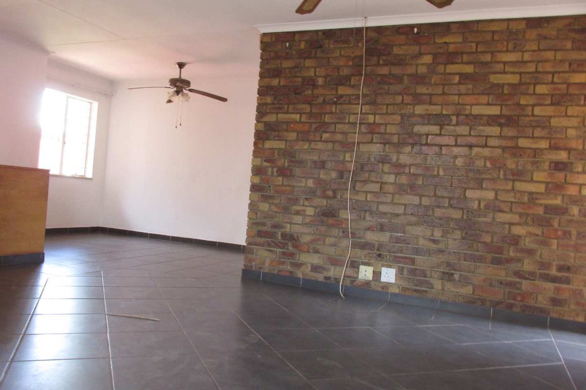 Spacious living area featuring a prominent exposed brick wall, dark tiled flooring, and dual ceiling fans in an open-plan layout.