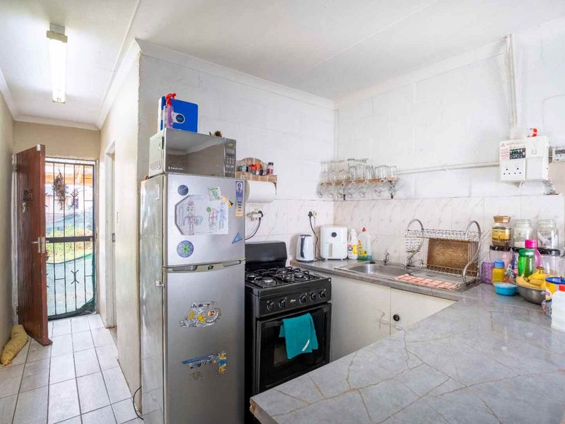 A compact kitchen featuring a gas stove, stainless steel sink, and laminate countertops, with direct access to an exterior security gate.