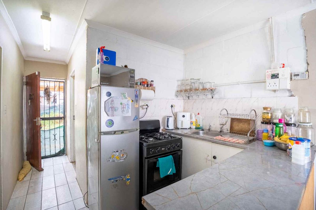 A compact kitchen featuring a gas stove, stainless steel sink, and laminate countertops, with direct access to an exterior security gate.