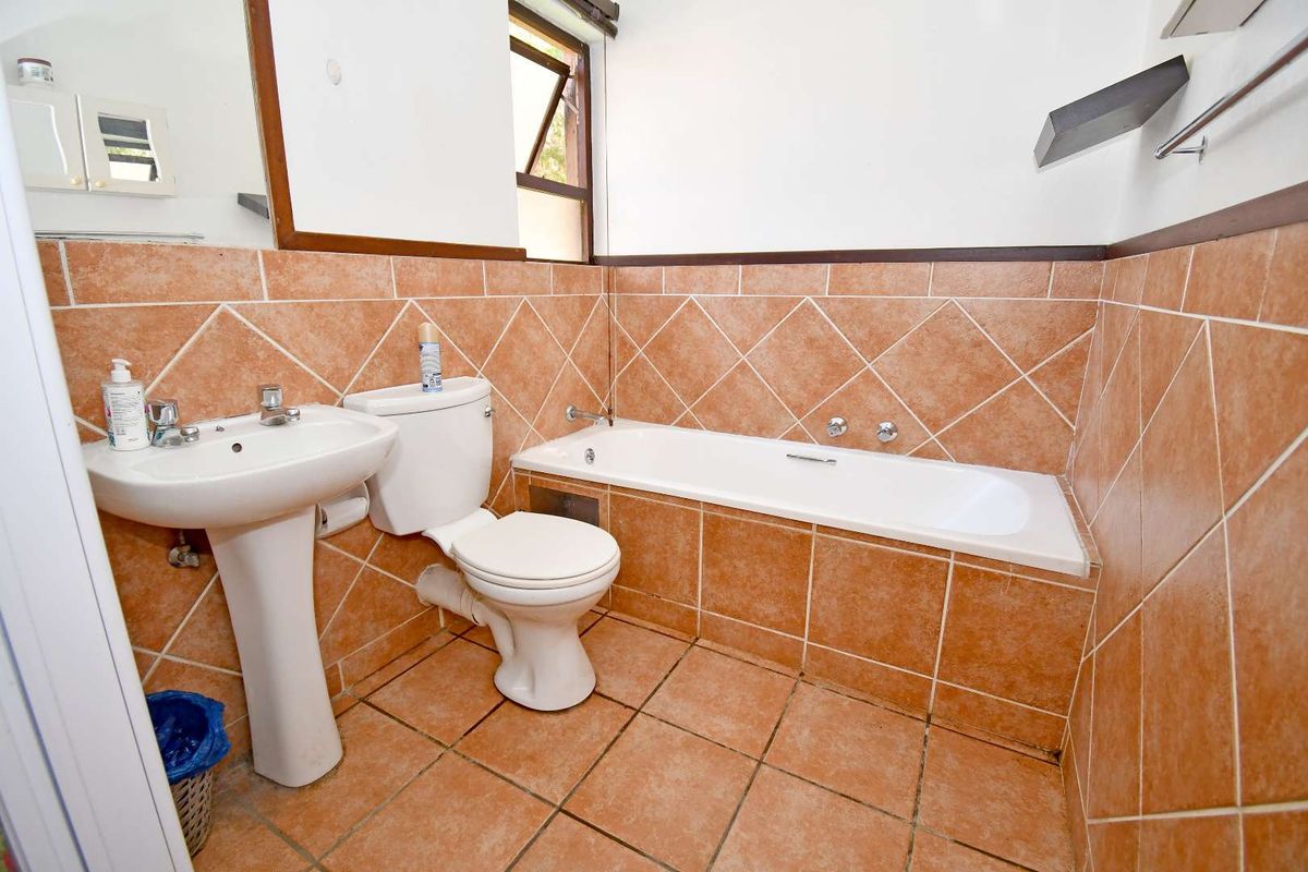A dated bathroom featuring terracotta-style wall and floor tiles, a pedestal basin, a standard toilet, and a built-in bathtub.