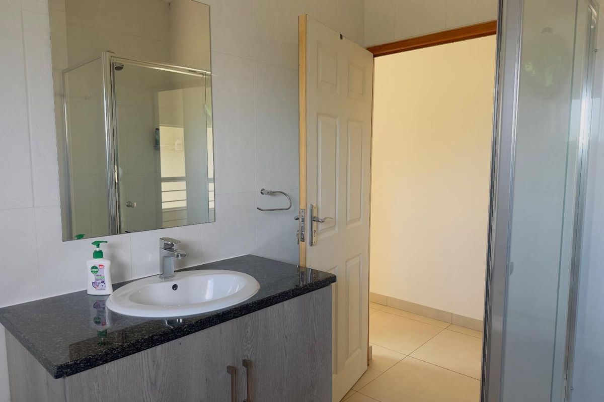 A functional bathroom featuring a modern vanity with a granite countertop, integrated basin, and a glass-enclosed shower stall.