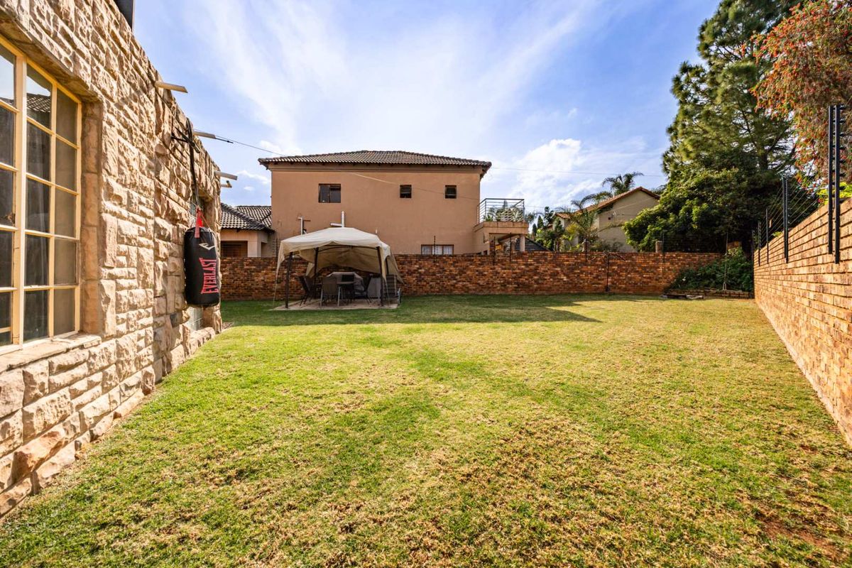 A spacious rear garden featuring a natural stone-clad exterior wall, a brick boundary wall, and a well-maintained lawn area.