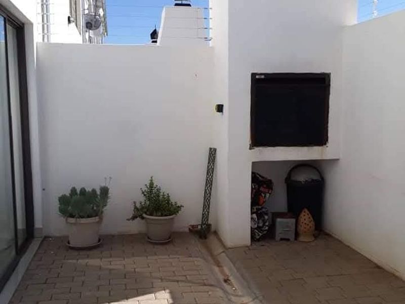A private paved patio area featuring a built-in braai, enclosed by white walls with electric fencing, suitable for outdoor entertaining.