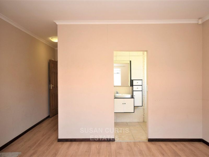 An empty bedroom featuring laminate flooring and a direct view into an adjoining bathroom with a built-in vanity and sink.