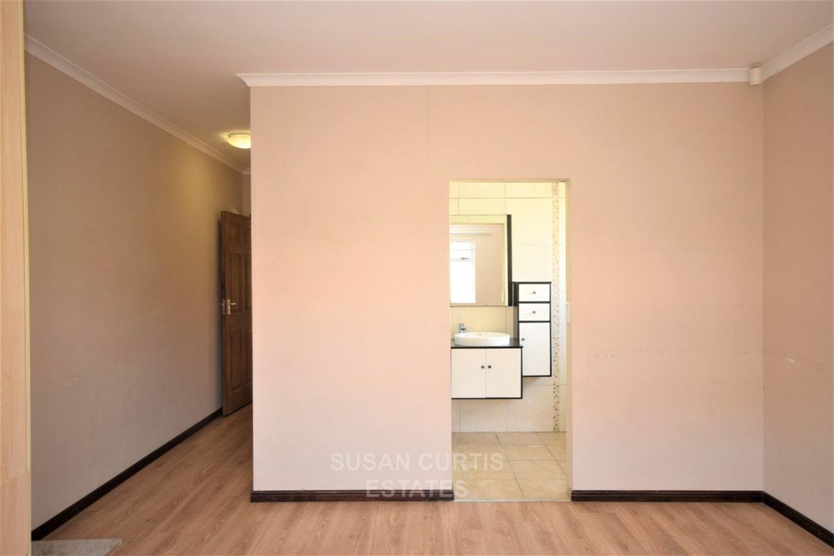An empty bedroom featuring laminate flooring and a direct view into an adjoining bathroom with a built-in vanity and sink.