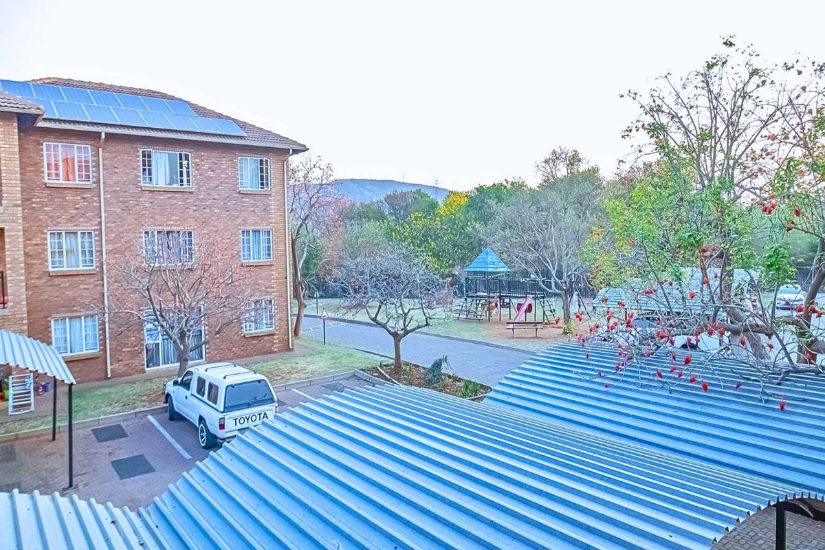 Elevated view of the apartment complex exterior, featuring brick facade, solar panels, paved parking area, and communal garden space with playground equipment.