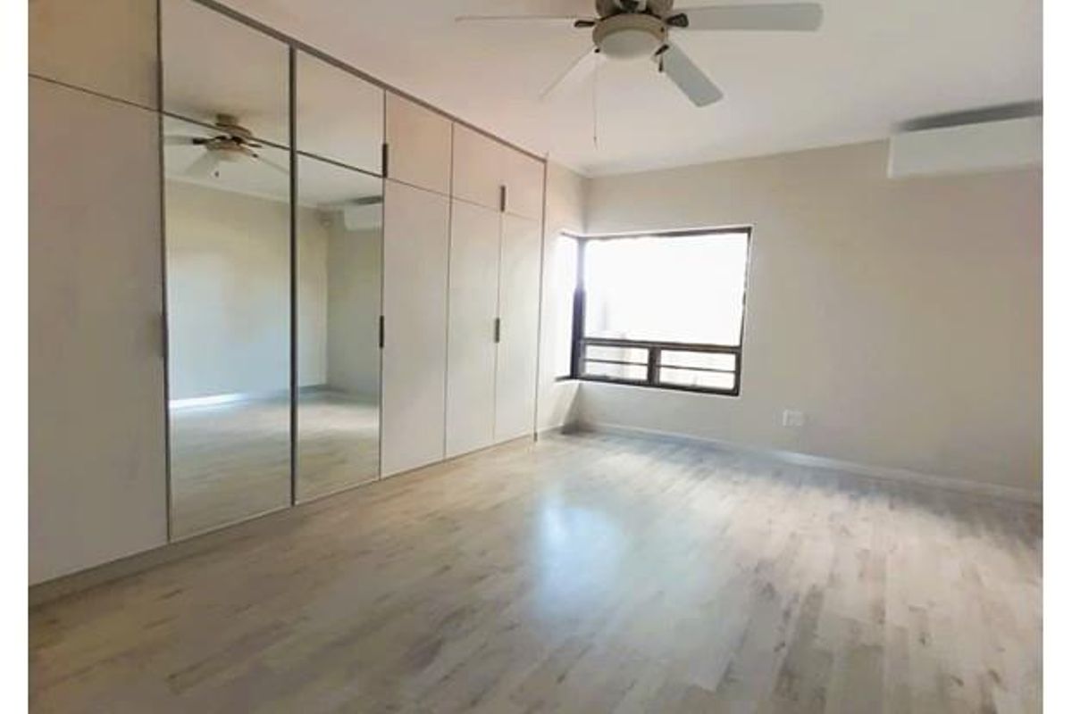 A spacious bedroom featuring extensive built-in cupboards with mirrored doors, a ceiling fan, and light-toned wood-look flooring.
