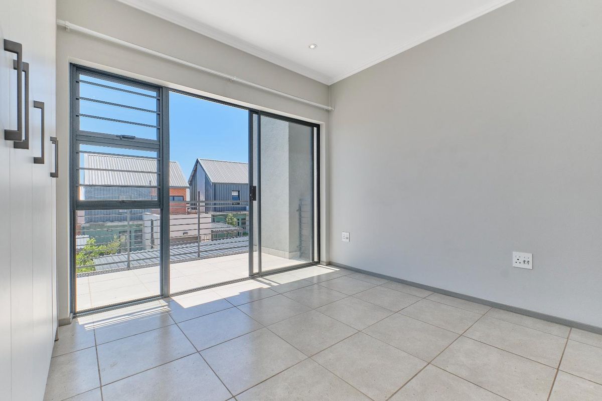 A bright, empty bedroom featuring neutral tiled flooring, built-in cupboards, and a large sliding glass door providing access to an outdoor balcony area.