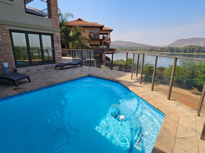 A well-maintained swimming pool area featuring stone paving, glass balustrades, and scenic waterfront views.