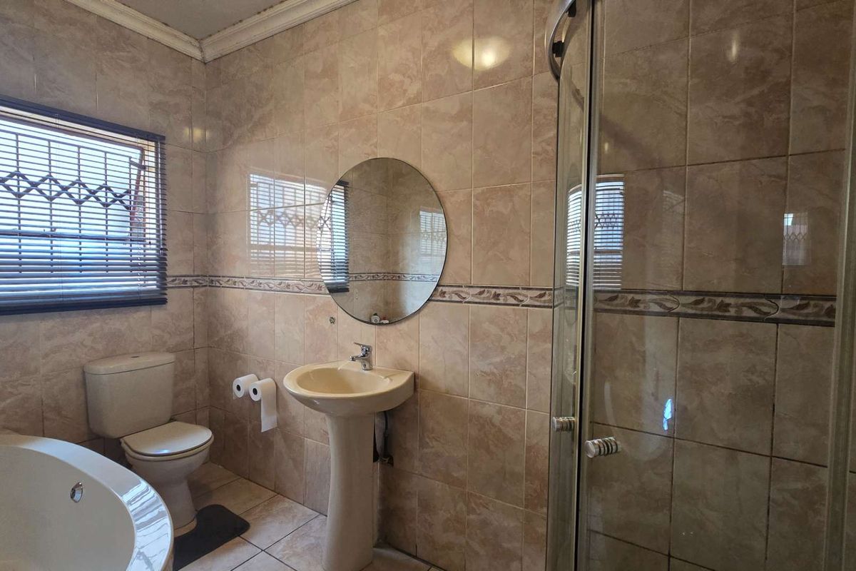 A functional bathroom featuring a corner bathtub, a separate shower enclosure, and a pedestal basin with neutral ceramic wall and floor tiling.