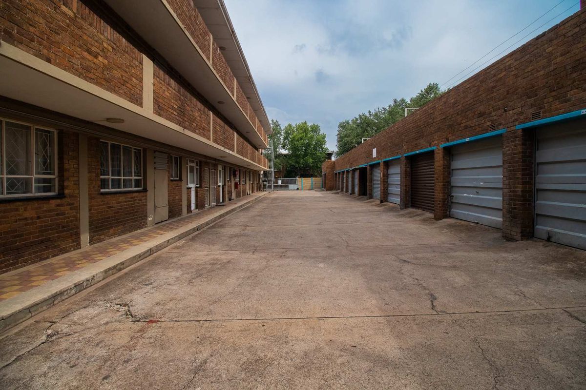 Exterior view of an apartment complex featuring a concrete driveway, brick facade, and a row of individual garage units.