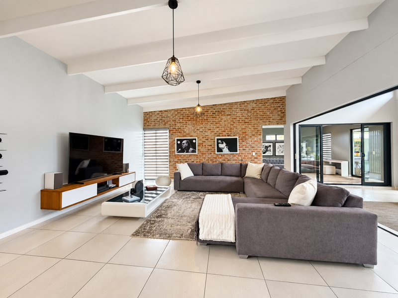Spacious living room featuring an exposed brick wall, vaulted ceiling with exposed beams, large format floor tiles, and seamless access to the outdoor patio.