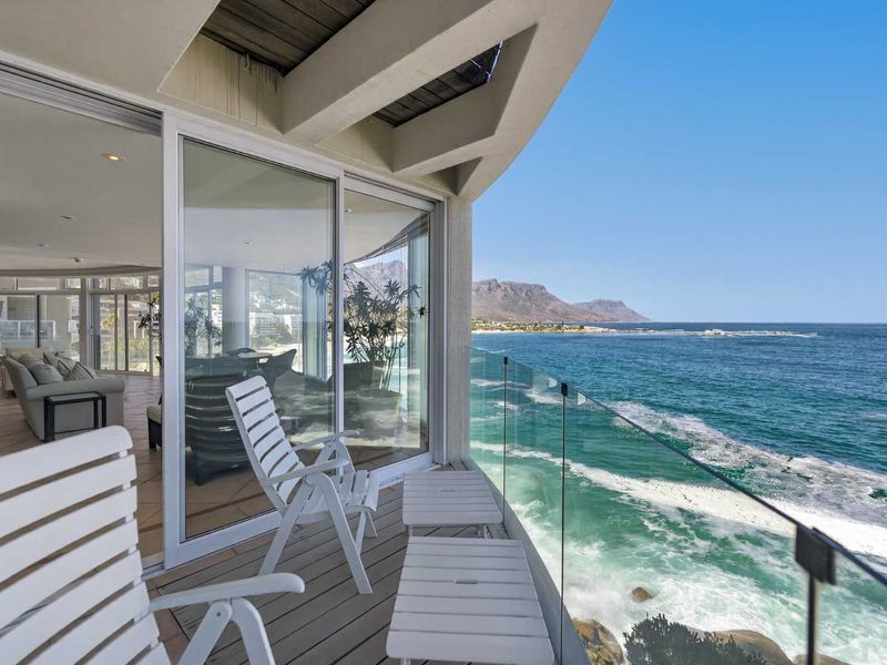 A spacious balcony featuring a modern glass balustrade and sliding doors, offering panoramic ocean views and seamless indoor-outdoor flow.