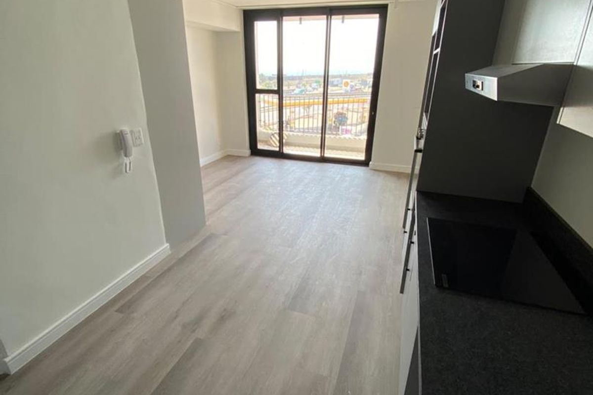 Modern open-plan living area featuring sleek cabinetry, stone countertops, integrated hob, and large sliding doors leading to a balcony with ample natural light.